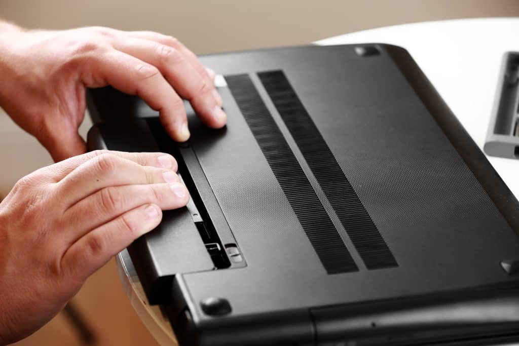 Repairman's hands removing the power battery from the laptop. Computer service and repair concept. Laptop disassembling in repair shop. Electronic development, electronic device fixing.